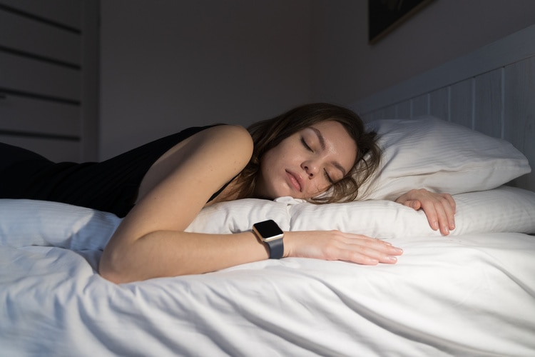 Kvinne som sover i sengen mens hun har på seg Apple Watch